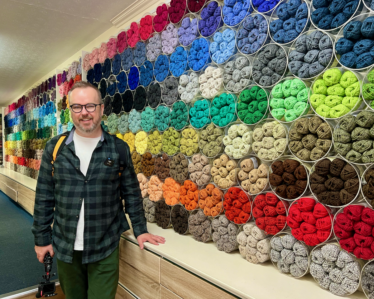 Patrick Hughes in front of a huge wall of varied yarn colours at Jamieson's of Shetland